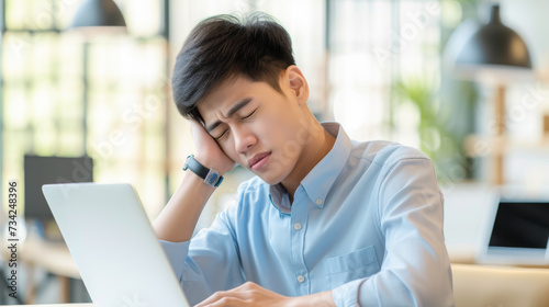 young man in business casual attire sitting at a desk, working on a laptop, and experiencing neck pain, likely due to poor posture or prolonged sitting.