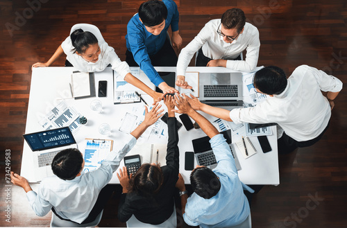 Top view diverse office worker join hand together in office room symbolize business synergy and strong productive teamwork in workplace. Cooperation and unity between business employee. Prudent