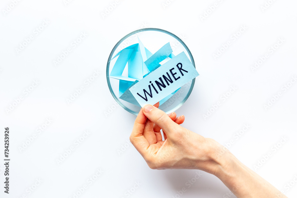 Female hand holding lottery ticket with winner word near glass bowl full of paper sheets. Winner concept Female hand holding lottery ticket with winner word near glass bowl full of paper sheets. Winner concept