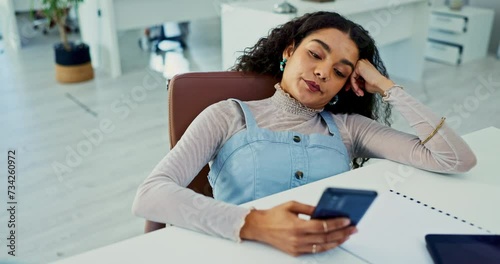 Phone, bored and tired with business woman at desk in office with fatigue or exhaustion from work. Mobile, burnout or social media distraction and frustrated or moody young employee in workplace photo