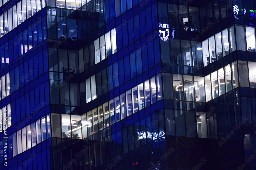 Fragment of the glass facade of a modern corporate building at night. Modern glass office in city.Pattern of office buildings windows illuminated at night.