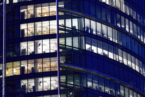 Fragment of the glass facade of a modern corporate building at night. Modern glass office in city.Pattern of office buildings windows illuminated at night.