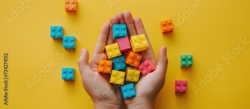 Hands holding colorful toy plastic bricks, blocks for building toys on yellow background photo