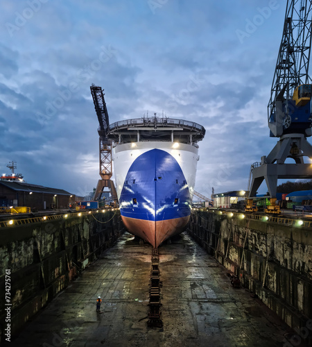 Large seismic offshore research ship in dry dock after painting hull surrounded with industrial cranes with water reflection