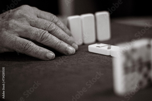 Close-up of an unrecognizable elderly person with wrinkles and veins playing a game of dominoes © Jordi