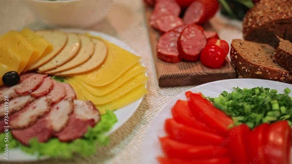 The abundance of food lying on the table. Slices of cucumbers, tomatoes, sausage, ham and meat spread out on plates. Grain bread and plates of salads lie nearby. The abundance of food lying on the table. Slices of cucumbers, tomatoes, sausage, ham and meat spread out on plates. Grain bread and plates of salads lie nearby.