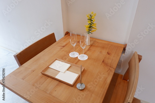 A desk, chairs and glasses for a couple with mimosa in a vase from the side