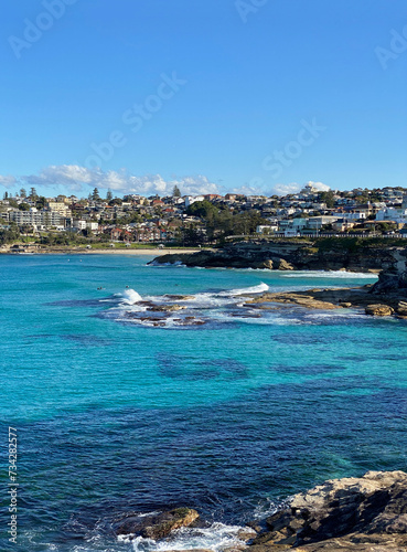 Bay and ocean coast with turquoise waves breaking on the beach. View of the town in the distance. Rocky ocean coast. Australian landscape and shoreline.