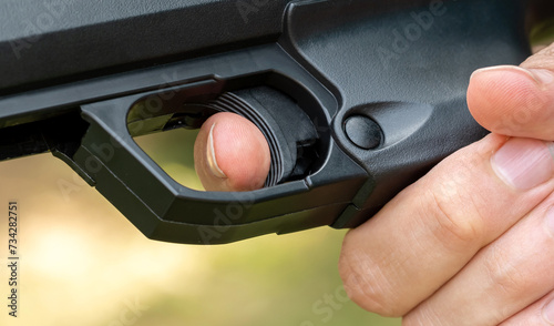 Detailed close-up of a persons index finger placed on the trigger of a black handgun, anonymous man ready to fire a simple sport firearm, air gun, firing a weapon. Gun safety rules, sports and weapons photo