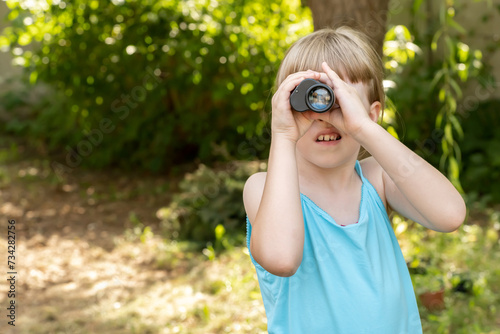 Young child uses binoculars to explore the garden, looking for something through the monocular, copy space searching, seeking, spying to find something. Curiosity and exploration simple concept © Tomasz