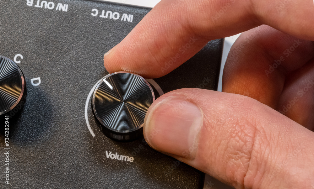 Anonymous man fingers finely tuning a volume knob on a sleek audio ...