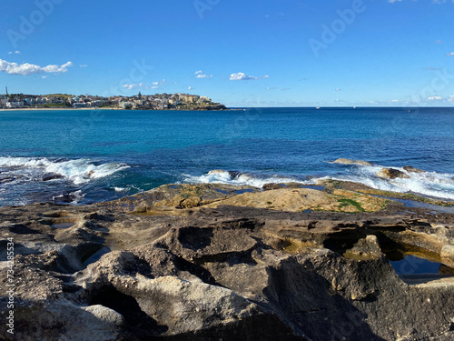 Bay and coast of the ocean. View of the city in the distance. Turquoise waves breaking on the rocky shore. Australia, NSW, landscape.