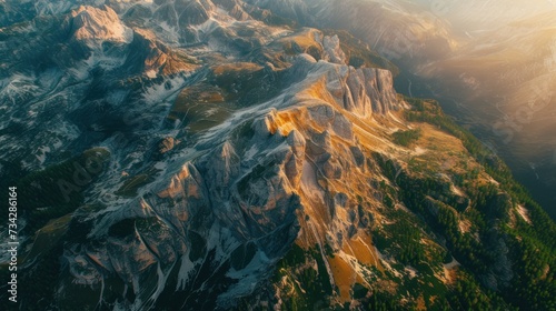 an aerial view of a mountain range with snow on the top and green trees on the bottom of the mountain.