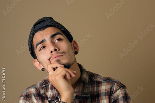 Portrait of young funny mexican migrant touch chin looking empty space deep thinking about his future isolated on khaki color background