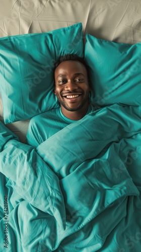 An overhead view of a man lying in bed underneath a green comforter.