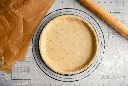 Unbaked Pastry Dough in a Tart Pan: Raw pie crust in a fluted pan on a floured work surface with a French rolling pin and unbleached parchment paper