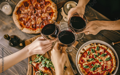 friends having a pizza party dinner with wine, top view. Group of people clinking glasses of red wine over rustic wooden table of Italian pizza