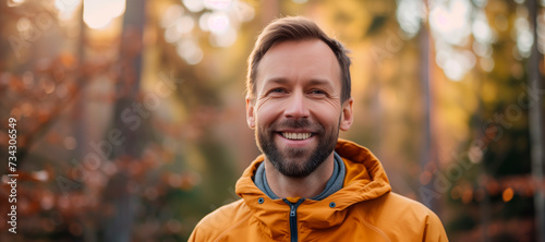 A portrait of a beautiful 34 year old man looking at the camera being happy, playful, wearing a colored hoodie, radiant, in nature