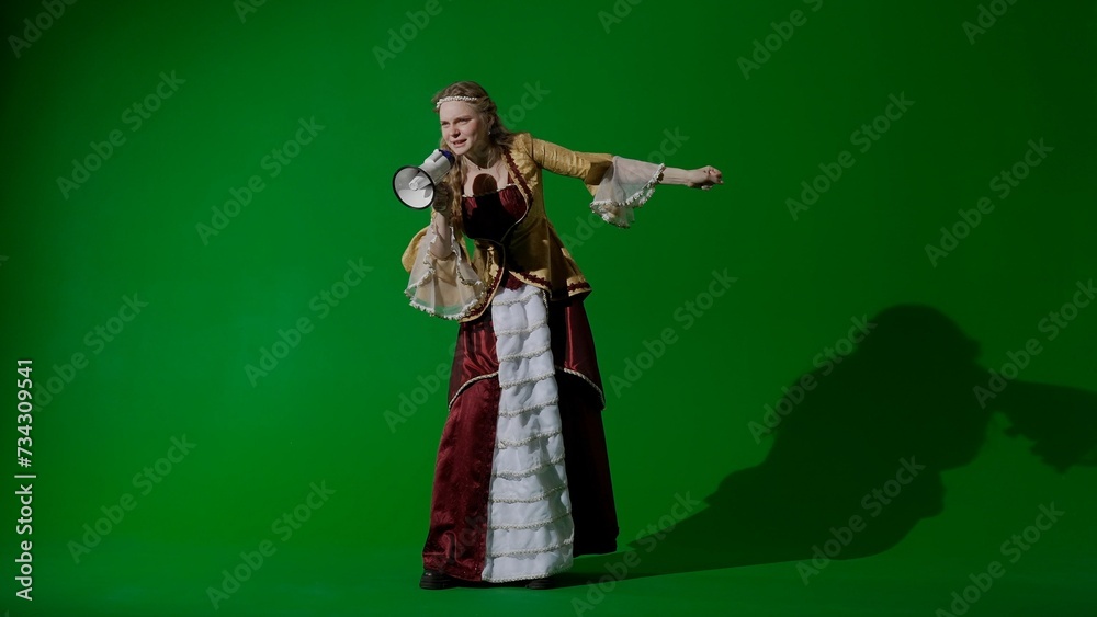 Fototapeta premium Woman in ancient outfit on the chroma key green screen background. Woman in renaissance dress holding megaphone and angrily shouting slogans at a protest.
