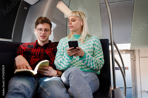 Couple is driving in a train or subway while reading a book and using a phone photo