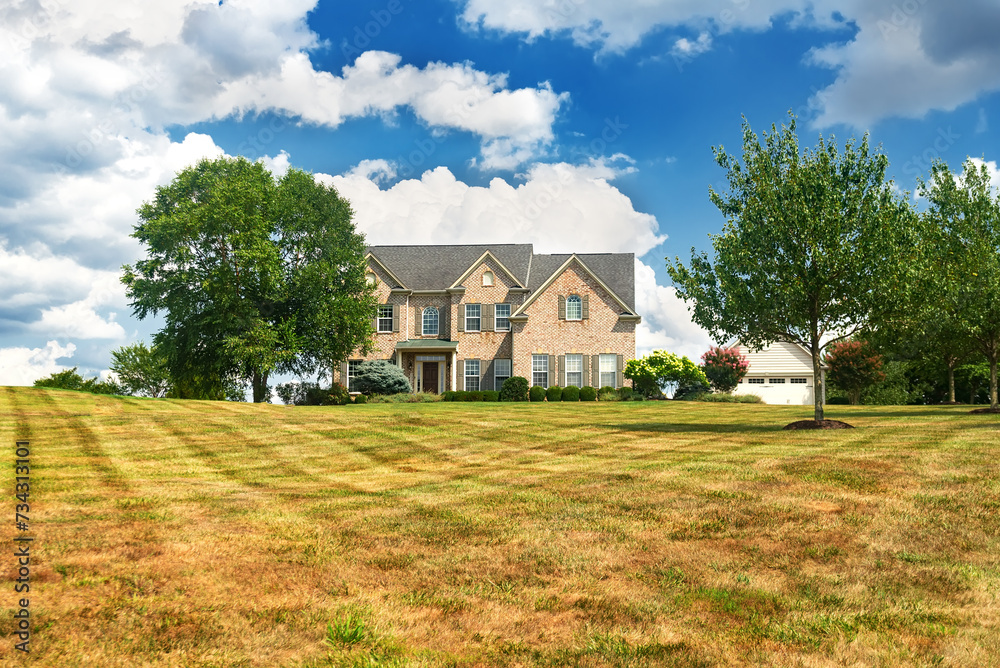 Brick country house with a large lawn against a background of blue clouds.