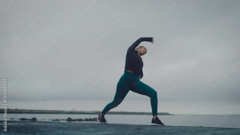Female stretching outside, exercising cardio workout training focused female athlete runner in cloudy seaside background tracking close up Female stretching outside, exercising cardio workout training focused female athlete runner in cloudy seaside background tracking close up