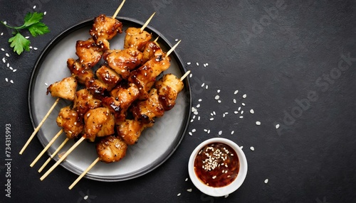 Teriyaki chicken skewers on plate over black background with copy space.