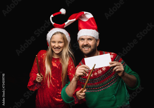 A young male music teacher teaches a girl in a red dress and Christmas hats to play the drums, the girl holds drumsticks in her hands, the concept of a music lesson in the studio on a black background