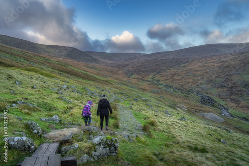 Mother and daughter walking on a trail in Glendalough with a view on a valley and stream. Hiking in beautiful autumn Wicklow Mountains, Ireland