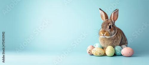 A bunny sits amidst colourful eggs against a blue background, evoking the festive spirit of the Easter holiday with ample copy space. Ai generative