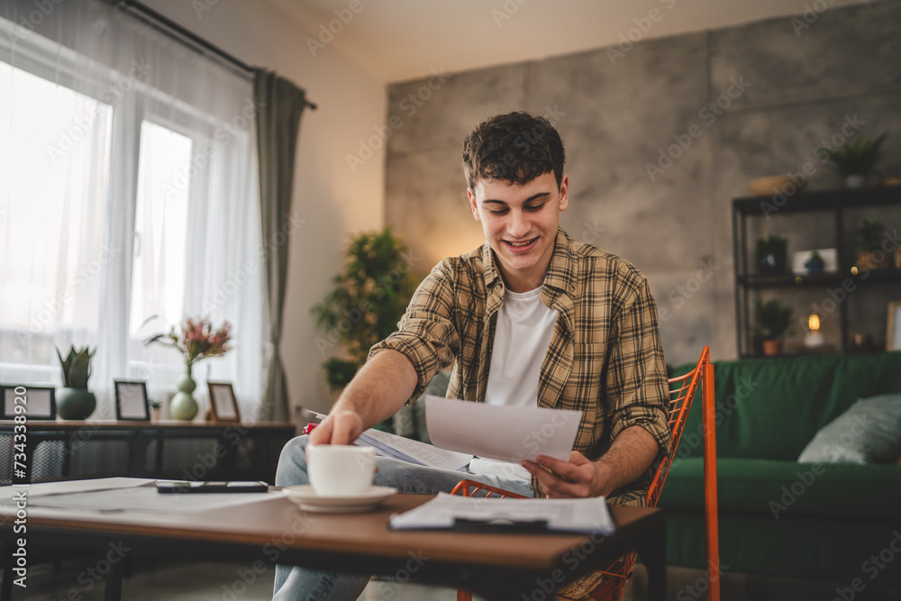 Young man hold paper read good news in letter sit at home received correspondence bank statement or notification invitation scholarship pleasant message or exam report