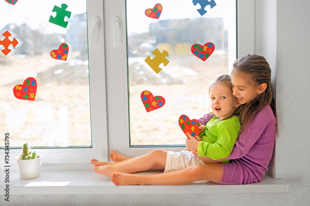 Φωτογραφία A girl with a little sister suffering from autism syndrome are sitting on the wi