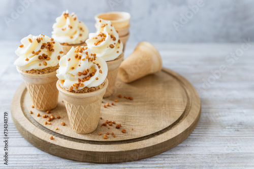 Cone cakes with cheese frosting and caramelized nuts on wooden board, ice cream alternative, party food for kids party photo