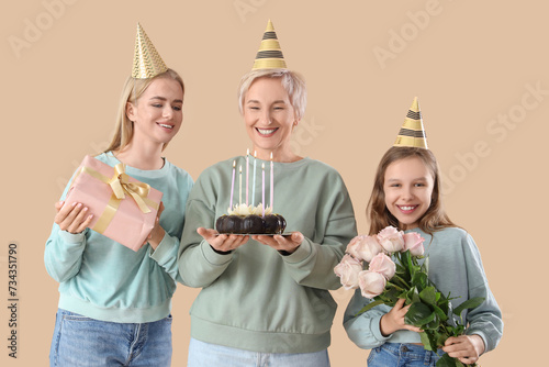 Little girl with her mom and grandmother celebrating Birthday on beige backgr...