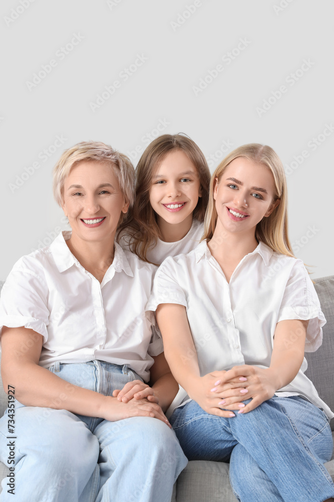 Little girl with her mom and grandmother sitting on sofa against light background Little girl with her mom and grandmother sitting on sofa against light background