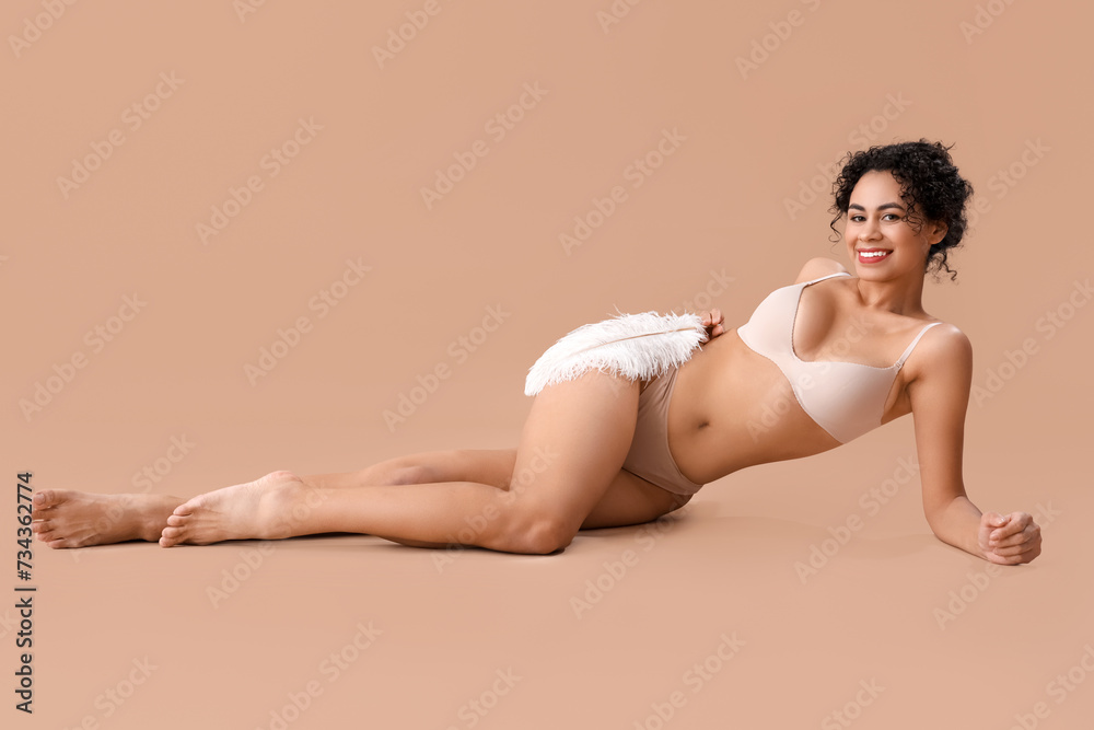 Beautiful African-American woman with soft feather on beige background. Hair removal concept Beautiful African-American woman with soft feather on beige background. Hair removal concept