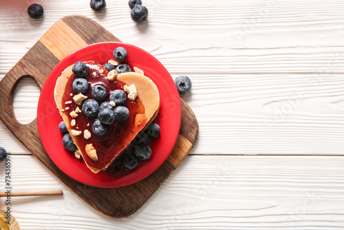Plate with tasty pancakes in shape of heart, blueberry and jam on light wooden background. Valentine's Day celebration