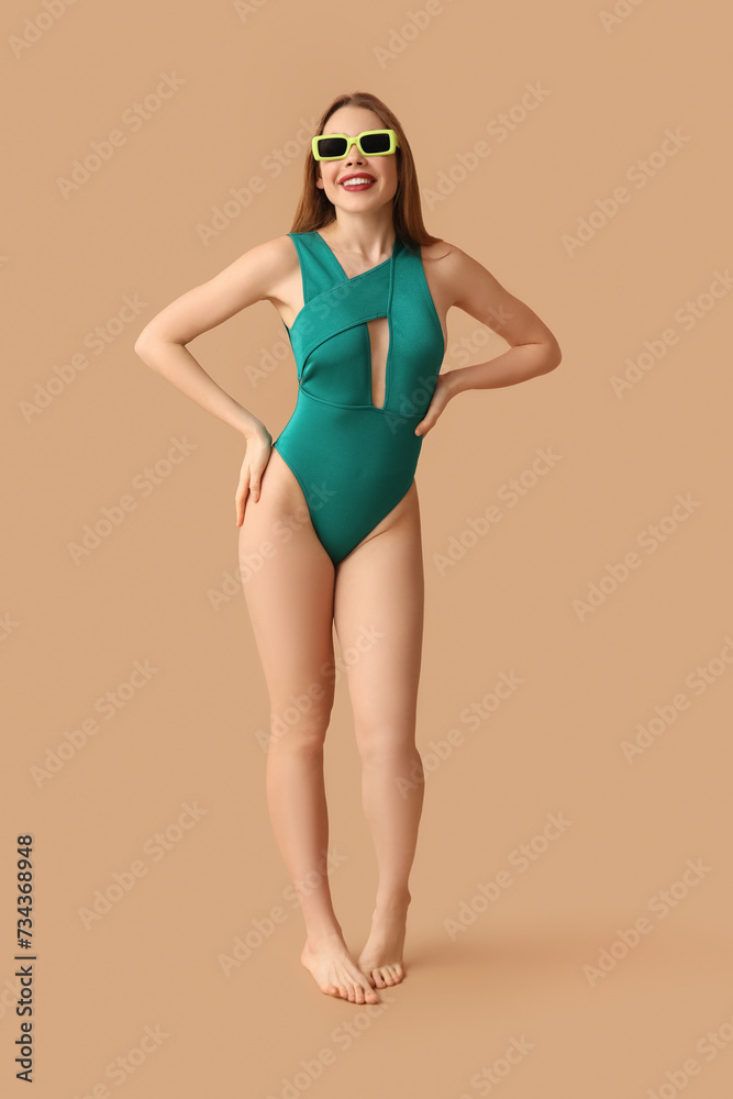 Pretty young woman in tank swimsuit on beige background Pretty young woman in tank swimsuit on beige background