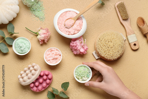 Female hand with different body scrubs and bath supplies on color background
