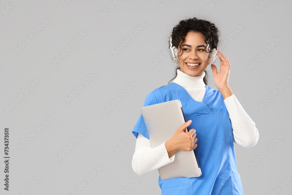 Female African-American medical intern in headphones with laptop on light background Female African-American medical intern in headphones with laptop on light background