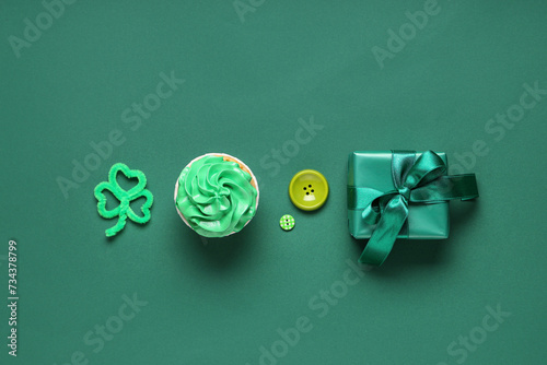 Tasty cupcake with gift box and decor for St. Patrick's Day on green background photo