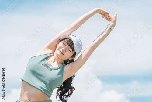 青空の中でストレッチをするアジア人女性（運動・スポーツ・ワークアウト・ボディメイク） 