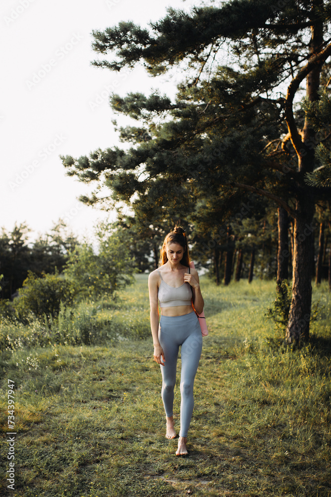Happy young woman in fitness clothes with yoga mat going to workout in the forest at sunset. Happy young woman in fitness clothes with yoga mat going to workout in the forest at sunset.