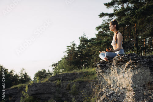 A young woman practices yoga and meditates in the mountains at sunset. Peace and unity with nature.