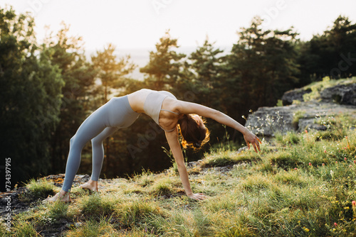 A young woman practices yoga in the mountains against the background of a pine forest.