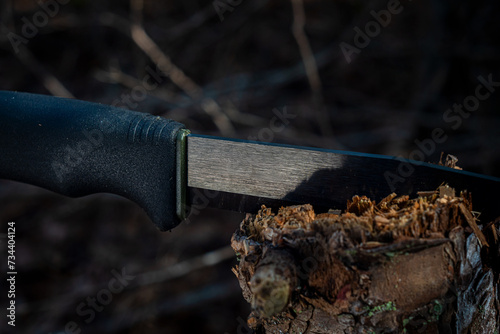 A black and green bushcraft survival knife out in the wilderness lodged in a fallen tree trunk