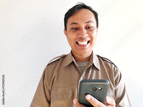 Smiling government employee showing smartphone screen. A young Asian civil servant wearing a khaki uniform.