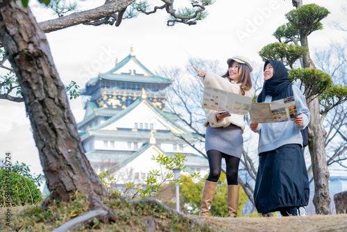 Travel, muslim travel, woman girl tourist Two Asian friends but different religions walking and visitor learning about history at Osaka Castle, landmarks in Japan and Osaka, holiday lifestyle.