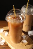 Refreshing iced coffee with milk in takeaway cups on table against black background, closeup