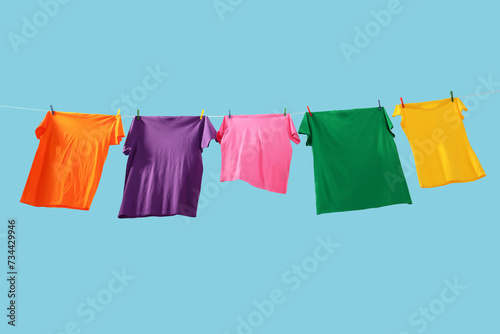 Colorful t-shirts drying on washing line against light blue background  low angle view